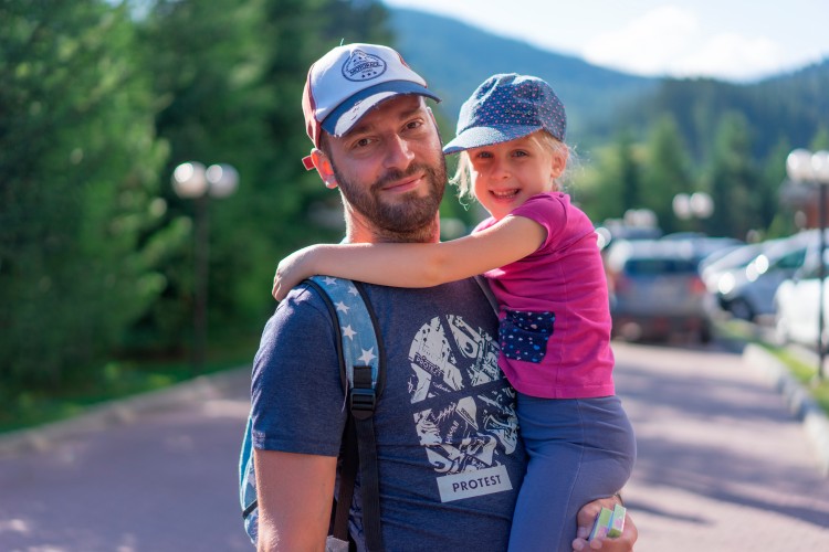 smiling-man-holding-daughter-on-the-nature-background